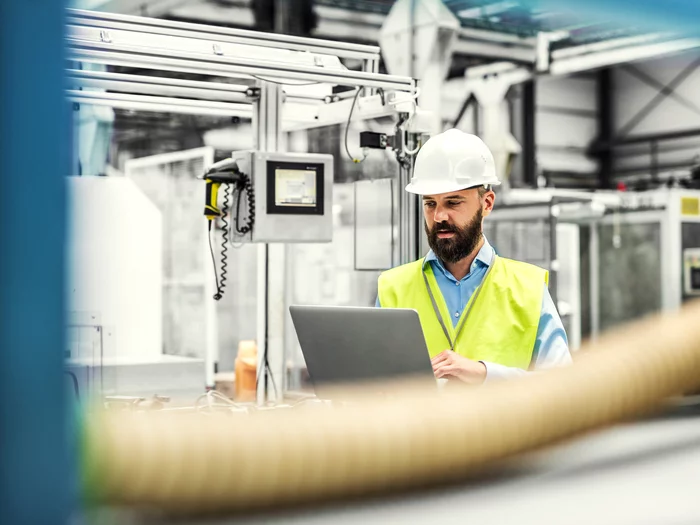 Foto: Gesco: Ein Mann in einer Fabrik, er überprüft Kleinteile auf einem Laufband an einer Maschine