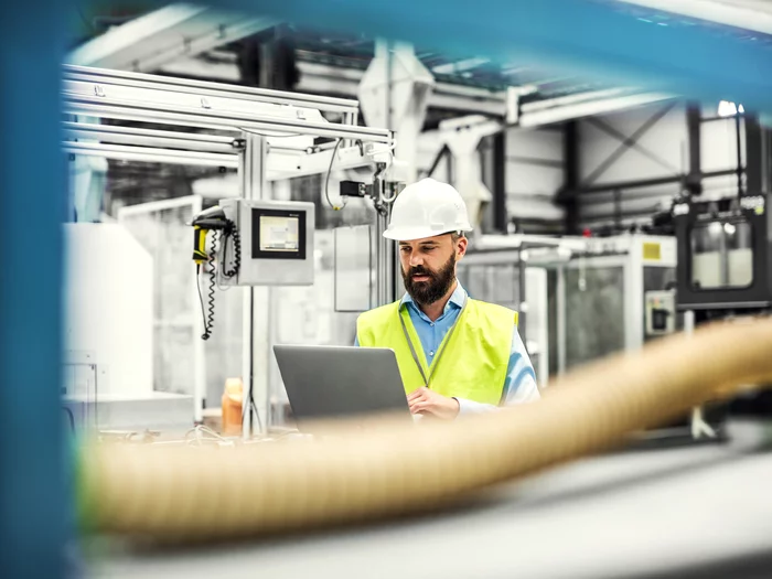 Foto: Gesco: Ein Mann in einer Fabrik, er überprüft Kleinteile auf einem Laufband an einer Maschine