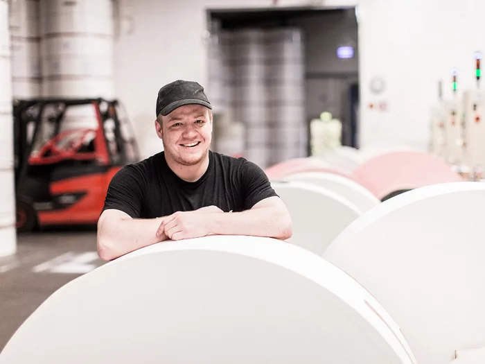 Foto: Gesco: Ein Mann mit Shirt laechelt, grosse weisse Rollen um ihn herum