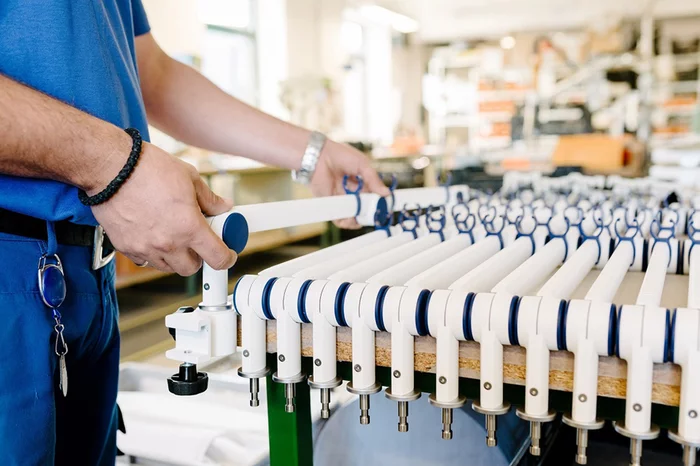 Foto: Gesco: Nahaufnahme von Haenden einer Person, sie in montiert an einer Produktionsmaschine mit laenglichen Komponenten